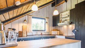 Una cucina moderna con travi in legno, una grande isola, luci a sospensione e una finestra che si affaccia sul verde.