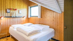 Una camera accogliente con pareti in legno, un letto con biancheria bianca, un tavolino e una finestra con tende.