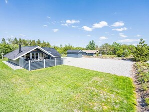 A residential area with a house featuring a sloped roof, a covered patio, and a gravel driveway.
