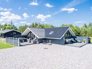 A modern house with a sloped roof, a patio with outdoor furniture, and a gravel driveway.