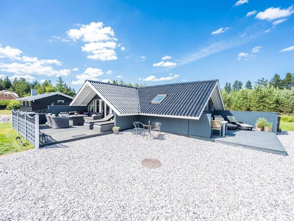 A modern house with a sloped roof, outdoor seating area, and a gravel driveway.