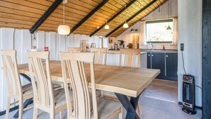 Zona pranzo con tavoli e sedie in legno, cucina con finestra e soffitto a vista con travi.