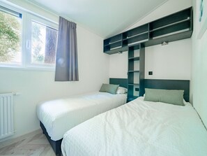 A room with two beds, a window with curtains, a radiator, and built-in shelving above the beds. - Forest Chalet Escape (Maarn)