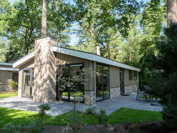 A modern house with a large glass door, a brick chimney, and a patio with outdoor furniture. - Forest Chalet Escape (Maarn)