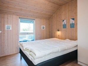 A room with wooden walls, a bed with white bedding, a window, and wall-mounted lights. - Holiday Home in Tarm (Tarm)