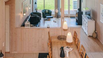 A spacious living area with a dining table, chairs, and a view of the outdoors through large windows.