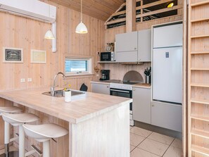 A kitchen with wooden walls, a central island with stools, a microwave, a stove, and a refrigerator. - Holiday Home in Tarm (Tarm)