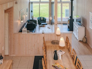 Uma sala de estar ampla com uma mesa de jantar, cadeiras, lareira e vista para o exterior.