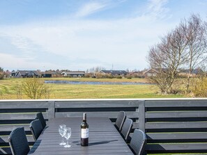 A dining table with chairs, a bottle of wine, and glasses on a deck overlooking a grassy field and houses. - Holiday Home in Tarm (Tarm)