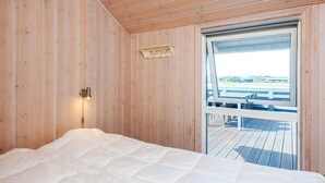A wooden cabin room with a bed, a wall-mounted light, a window with a view of a dock, and a small shelf with a nameplate. - Holiday Home in Tarm (Tarm)