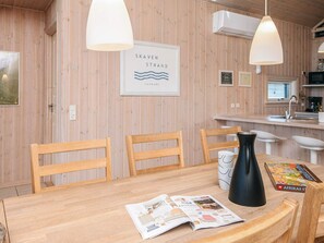 A wooden interior with a dining table, chairs, a black vase, a magazine, and a framed sign reading 'SKAVEN STRAND DANMARK'. - Holiday Home in Tarm (Tarm)
