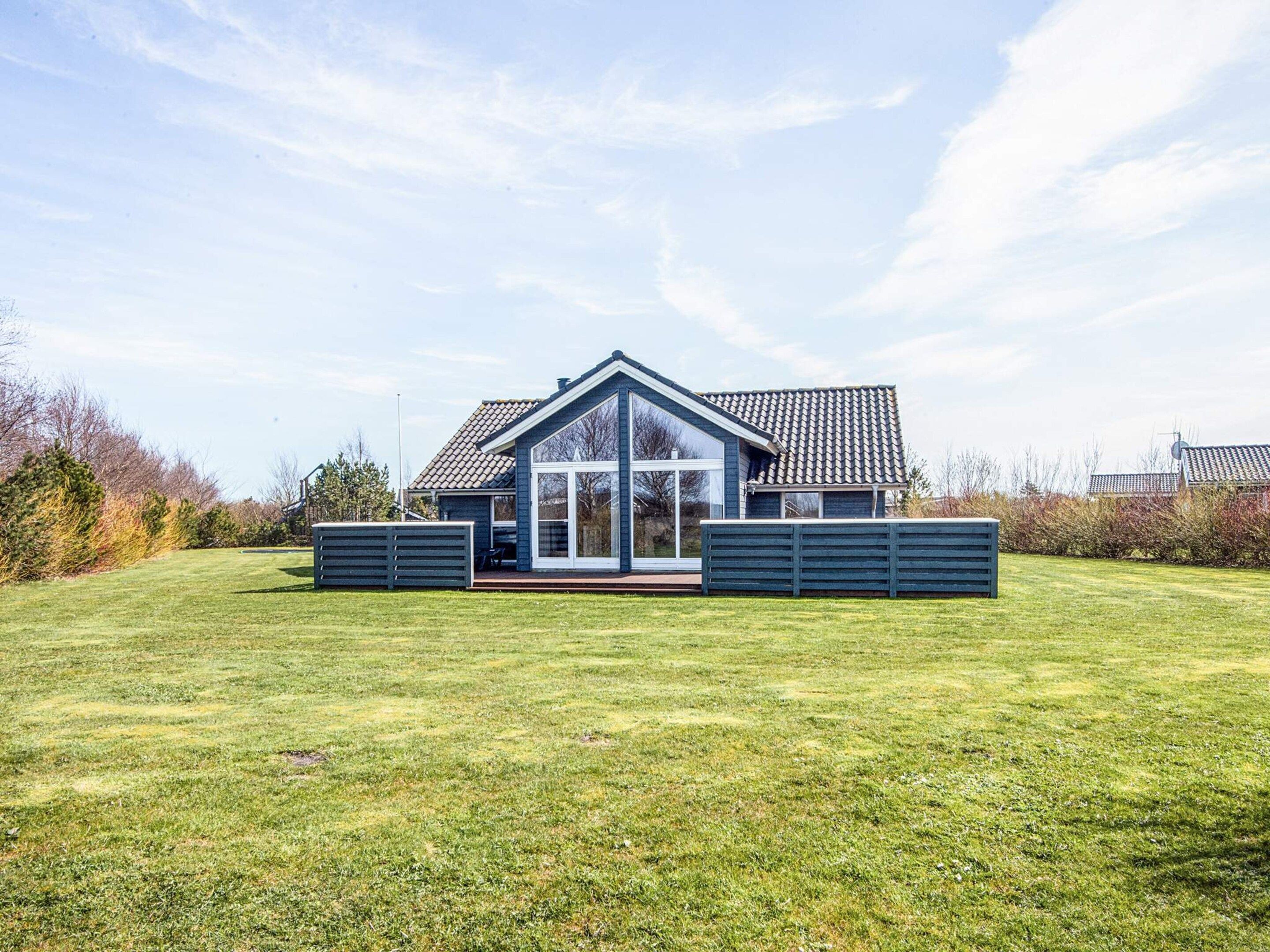 A modern house with a large glass front, a sloped roof, and a well-maintained lawn.