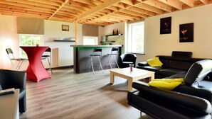 Uma sala de estar moderna com teto de madeira, um sofá de couro preto, uma mesa vermelha e uma área de cozinha com balcão.