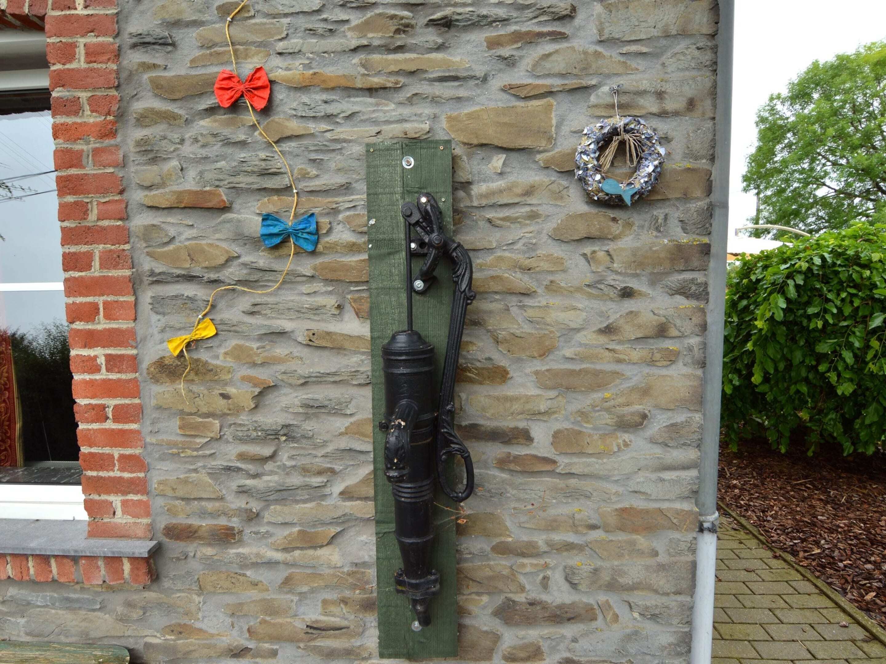 A stone wall with a wooden post, a metal hook, and decorative bows.