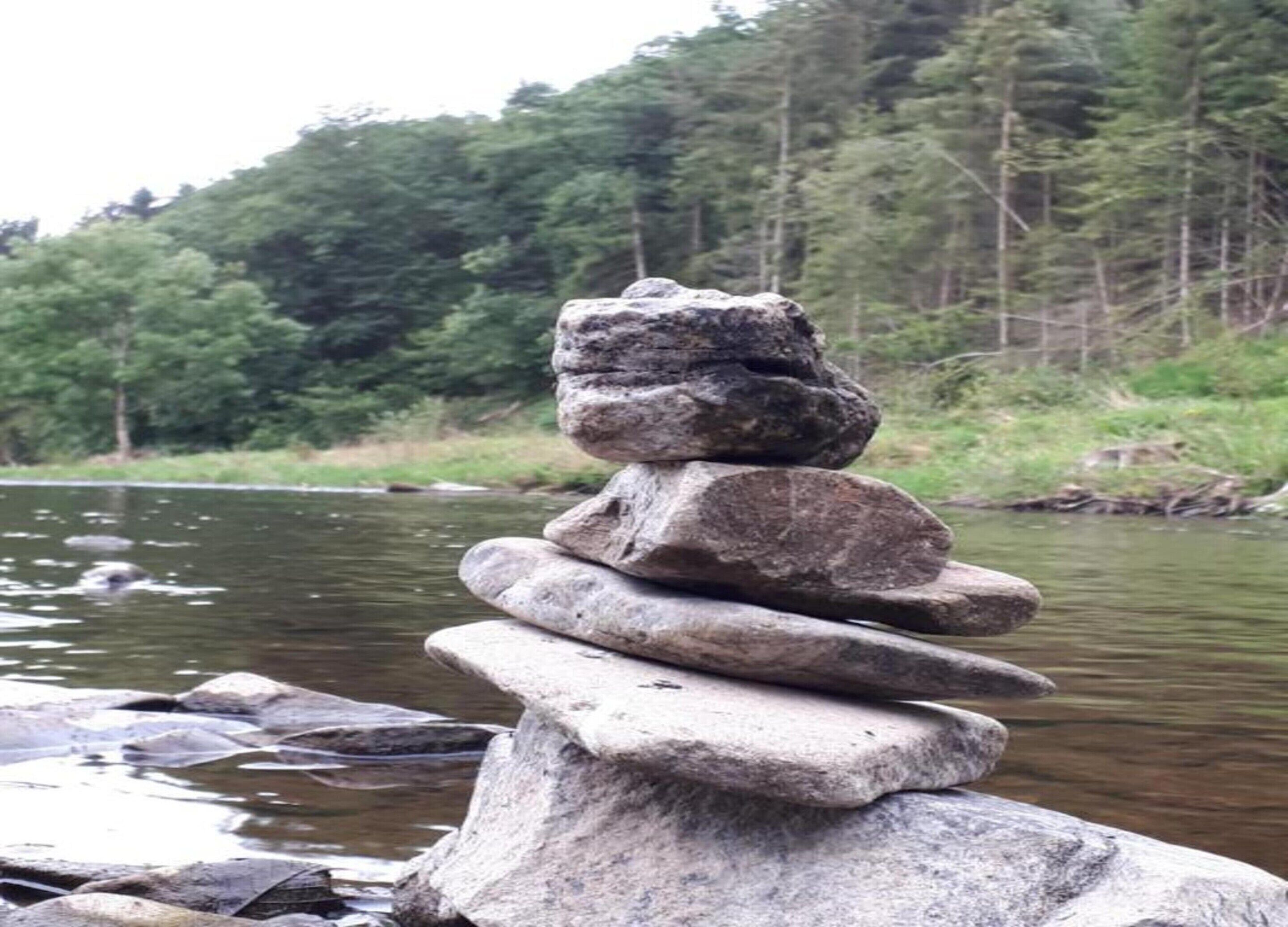 A stack of stones by a calm river with a forest in the background.