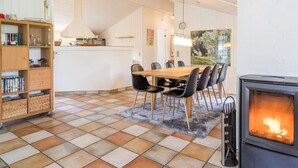 A dining area with a wooden table and chairs, a bookshelf, a kitchen area with a microwave, and a fireplace. - 4 Star Holiday Home in Henne (Henne)