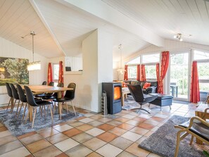 Een gezellige woonkamer met een open haard, een eethoek met een houten tafel en stoelen, en een bank met rode gordijnen.