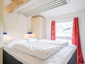 A bedroom with a bed, a window with red curtains, and a ceiling fan.