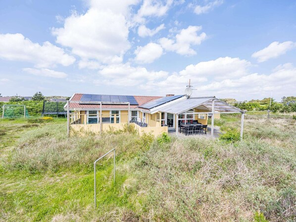 Une maison équipée de panneaux solaires, une terrasse avec des meubles d’extérieur et une cour clôturée.
