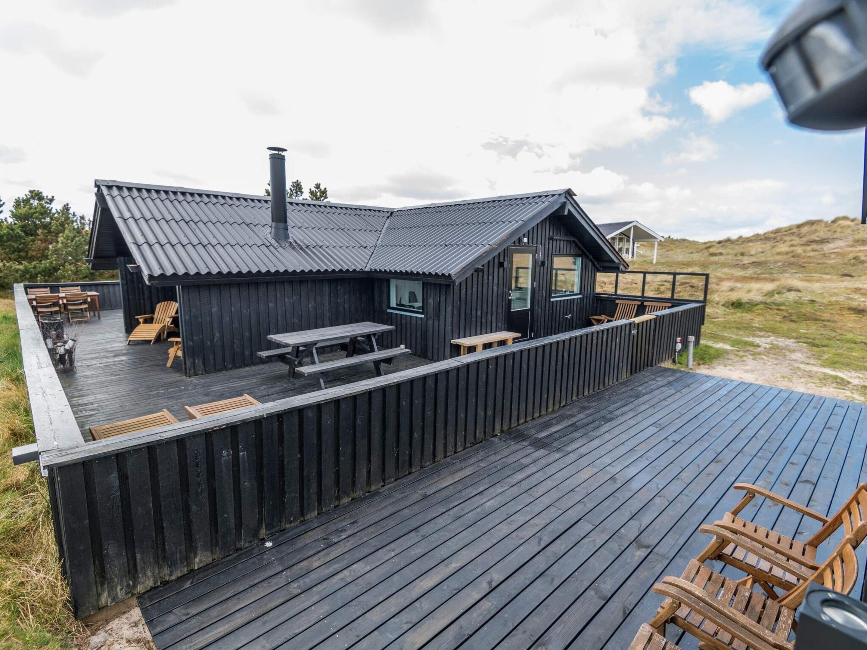 A wooden deck with outdoor seating and a building with a dark roof.
