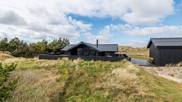 Une cabane moderne, de couleur noire, avec un toit en pente, une terrasse et un petit espace extérieur aménagé pour s’asseoir.