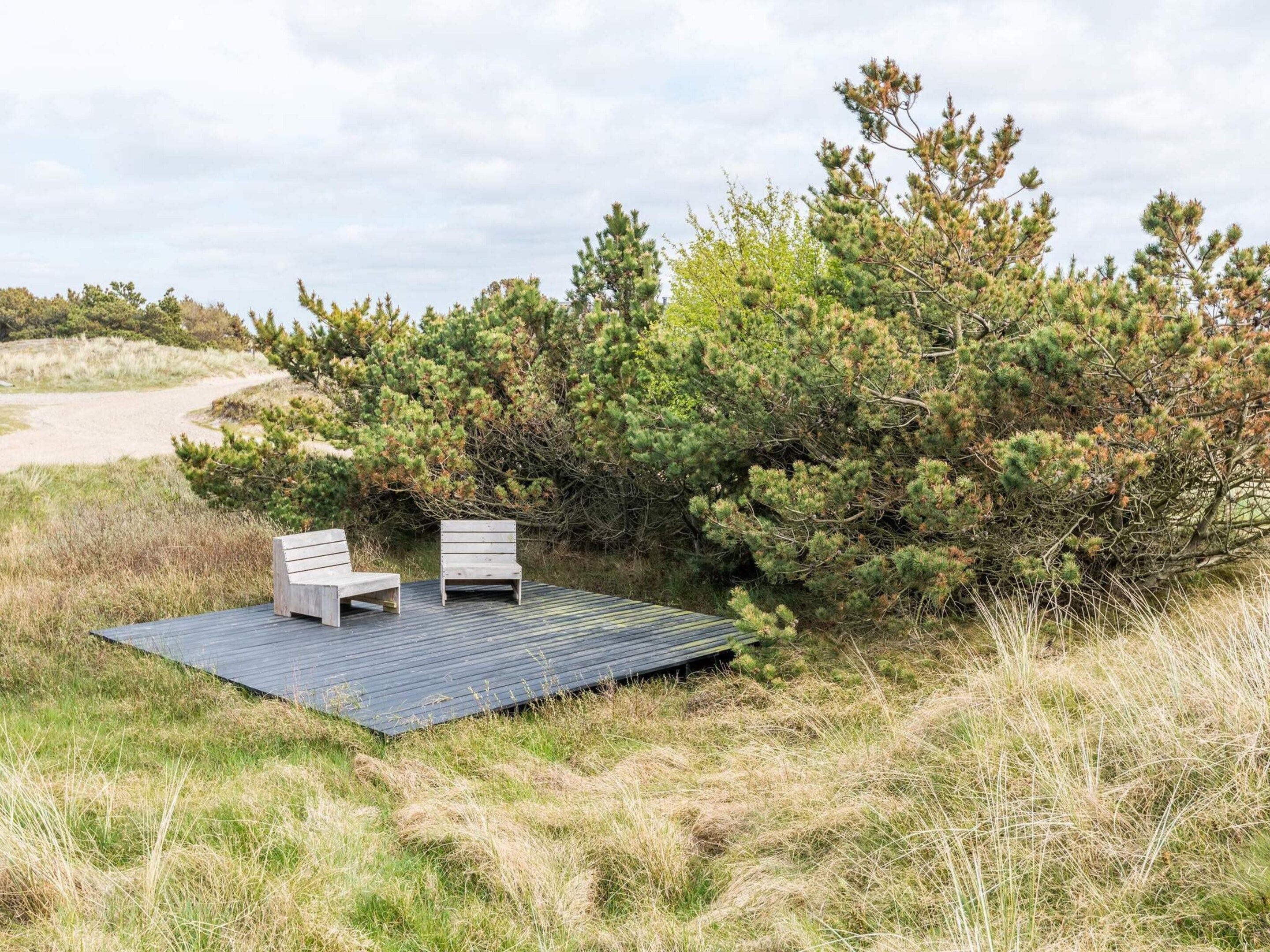 Una terraza con dos sillas de madera y vista a un paisaje natural con árboles y un sendero arenoso.
