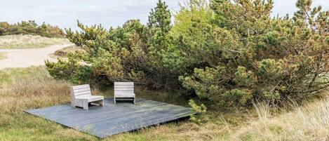 Una terraza con dos sillas de madera y vista a un paisaje natural con árboles y un sendero arenoso.