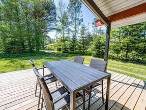 A wooden deck with a table and chairs, surrounded by lush greenery and trees. - 4 Person Holiday Home in Norre Nebel (Norre Nebel)