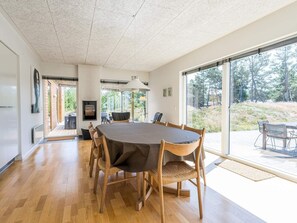 Uma sala de jantar espaçosa com uma grande mesa redonda, cadeiras de madeira e vista para um jardim através de grandes portas de vidro deslizantes.
