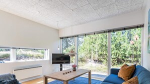 A modern living room with a large window, a flat-screen TV, a wooden coffee table, and a blue sofa with cushions. - 6 Person Holiday Home in Henne (Henne)