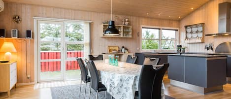 A spacious kitchen with a dining area, wooden walls, and large windows.
