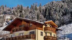 A two-story chalet with wooden balconies, set against a snowy mountain backdrop. - Apartment Grossarl Near Ski Slopes (Grossarl)