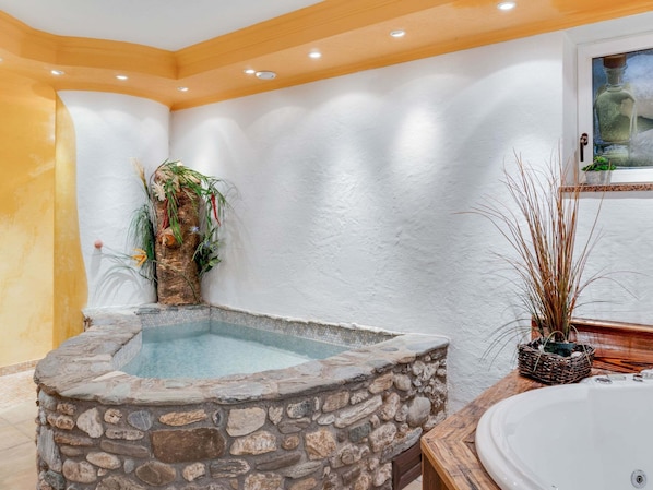 A stone hot tub in a room with a white wall and a wooden ceiling.