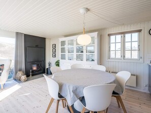 A dining area with a round table, white chairs, a white cabinet with glass doors, a fireplace, and a window with blinds.