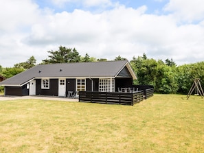 A black building with a sloped roof, a covered outdoor seating area, and a swing set in a grassy field. - 4 Star Holiday Home in Tarm (Tarm)