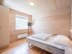 A bedroom with a bed, a window, a television, and wooden paneling.