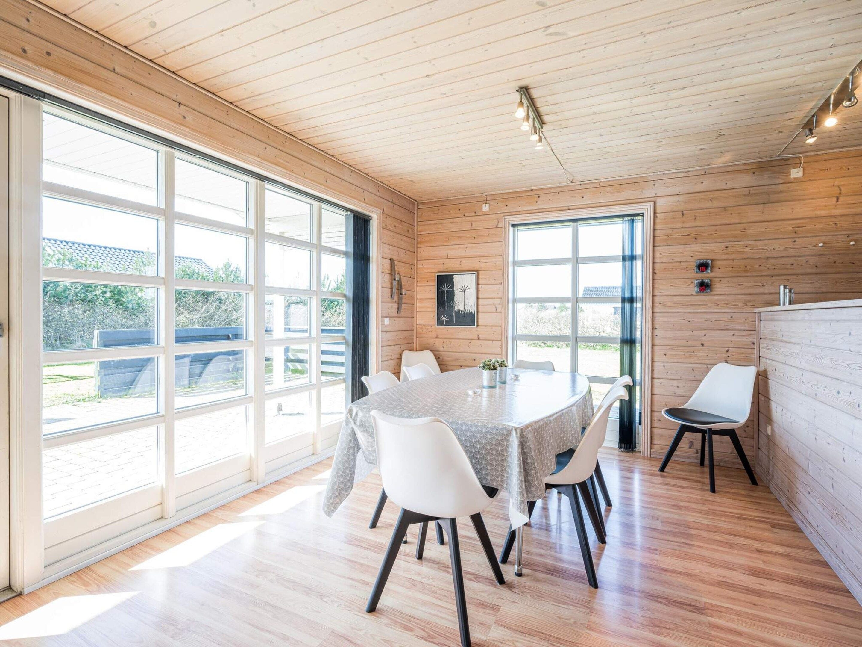 A spacious room with a large dining table, white chairs, and a wooden ceiling.