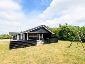 A single-story building with a large windowed porch, surrounded by a grassy yard and a swing set. - 4 Star Holiday Home in Tarm (Tarm)