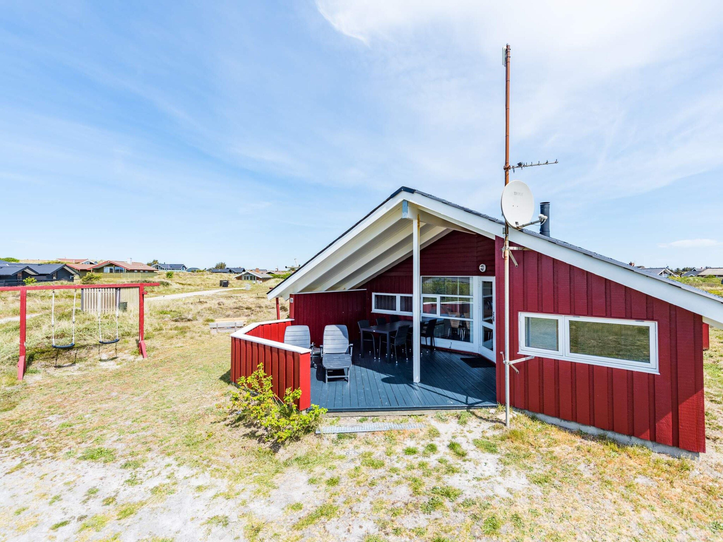 A red building with a covered outdoor area, a satellite dish, and a swing set.