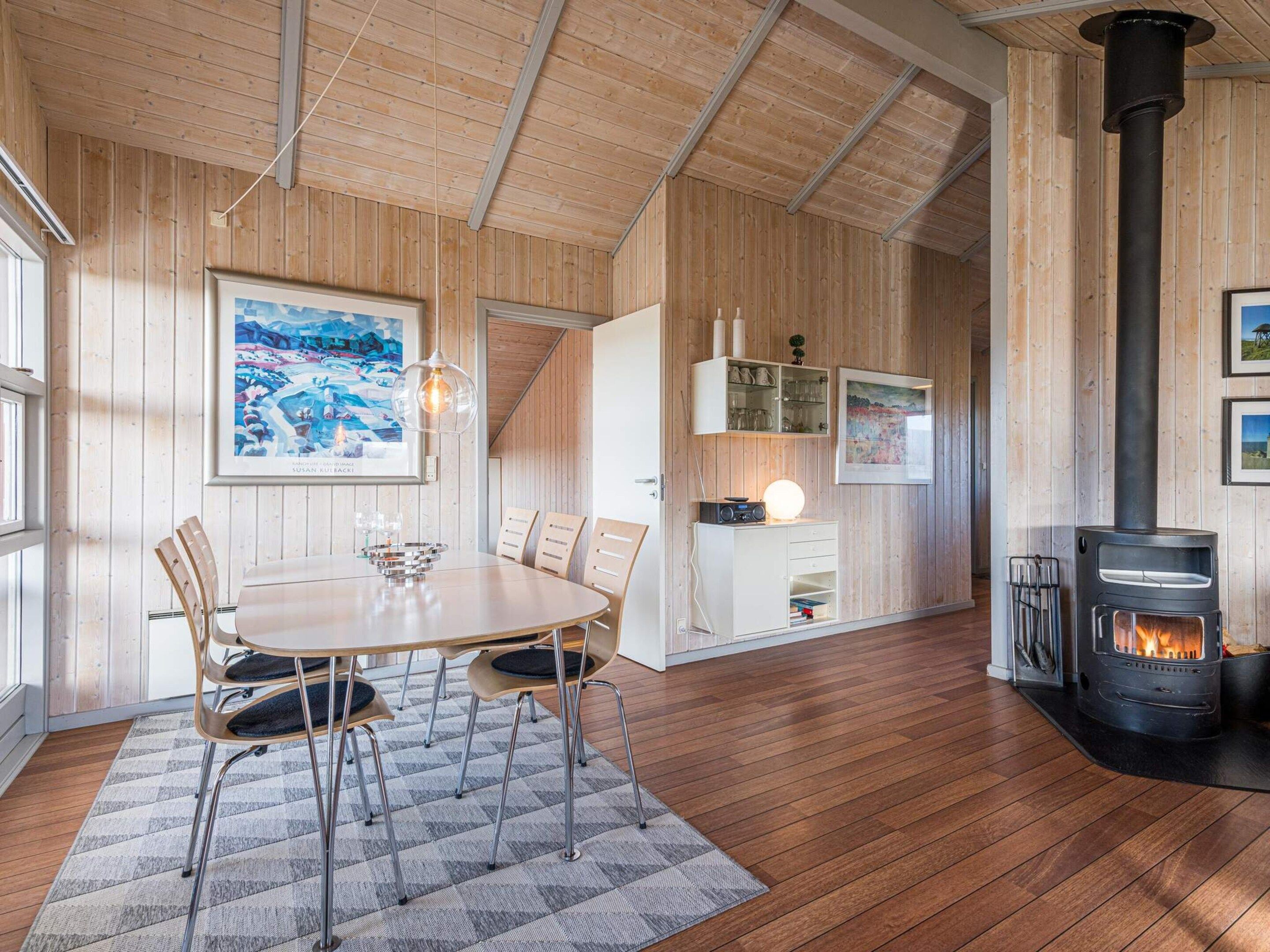 A cozy room with a wooden floor, a dining table with chairs, a fireplace, and a wall-mounted cabinet with a radio.