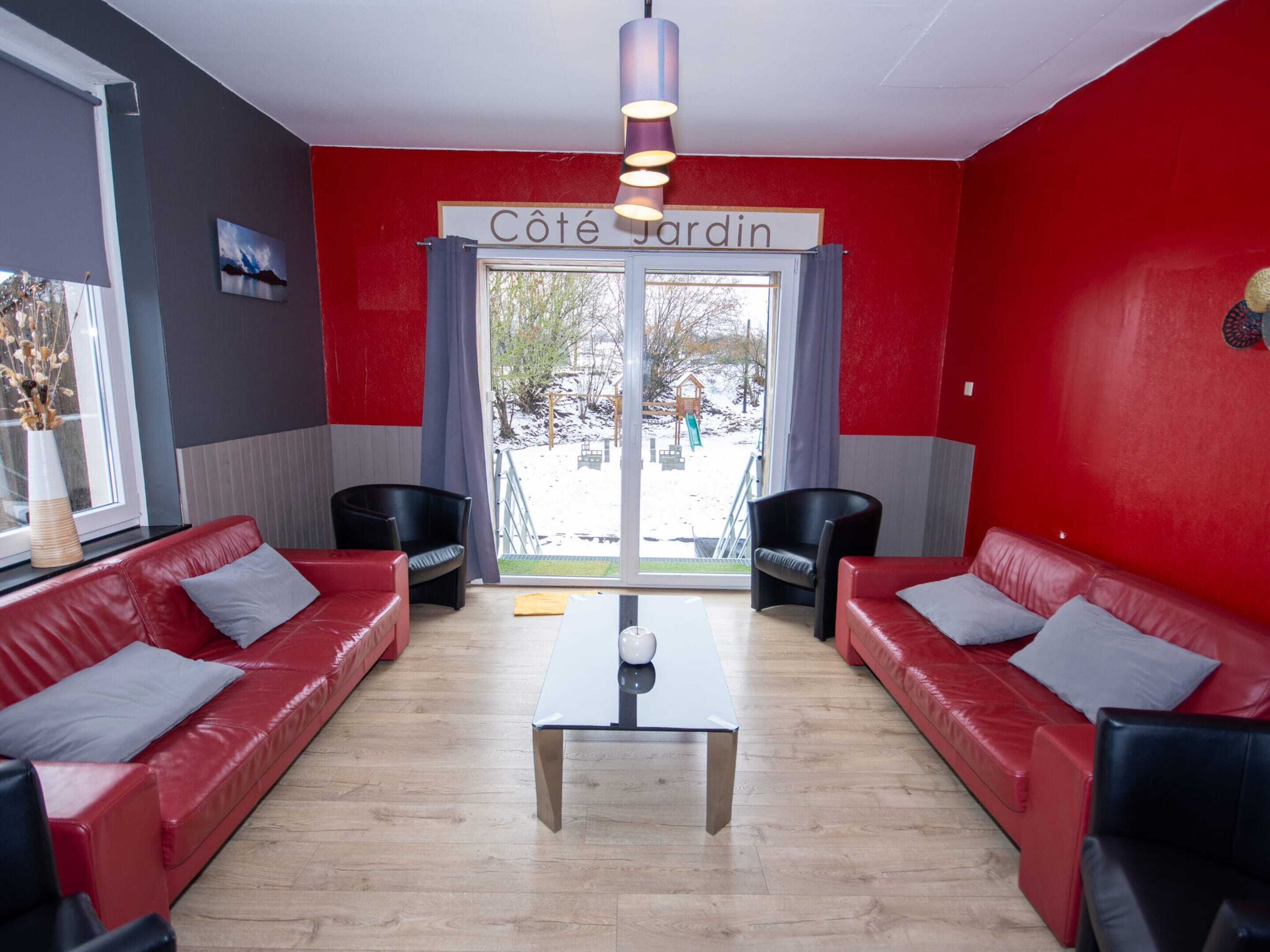 A room with red walls, a large window, two black chairs, and a red sofa.