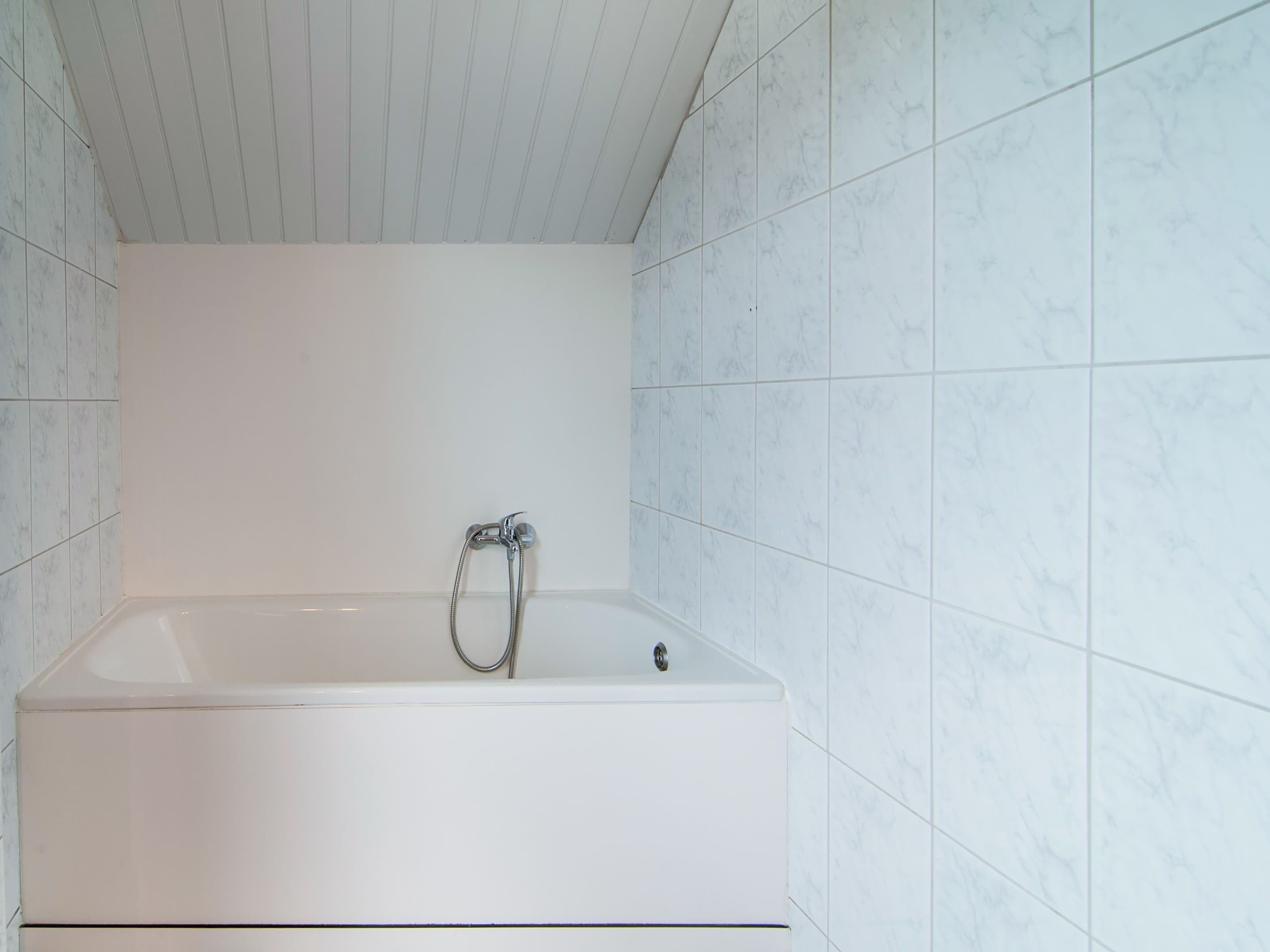 Un baño con una bañera blanca, paredes cubiertas de azulejos blancos y un techo blanco.