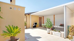A covered outdoor patio with a TV, seating, and potted plants. - Beachside Getaway w/ Garden (Noto)