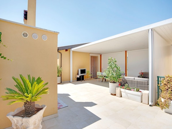 A covered outdoor patio with a TV, seating, and potted plants.