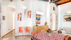 A dining area with a table covered by a patterned tablecloth, orange chairs, and a wooden cabinet with decorative items. - Beachside Getaway w/ Garden (Noto)