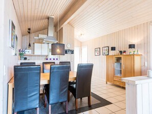 A modern kitchen with wooden paneling, a dining area with black chairs, and a wooden cabinet with glass doors.