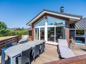 A modern house with a deck, a dining area with chairs, and a large glass door leading to an outdoor space.