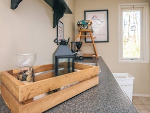 A kitchen counter with a coffee maker, a wooden tray, and a framed picture on the wall.