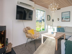 A living room with a fireplace, a sofa, a coffee table, a TV mounted on the wall, and a window with a view of greenery. - 4 Star Holiday Home in Hemmet (Hemmet)