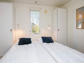 A bedroom with a bed, two bedside lamps, a window, and a door.